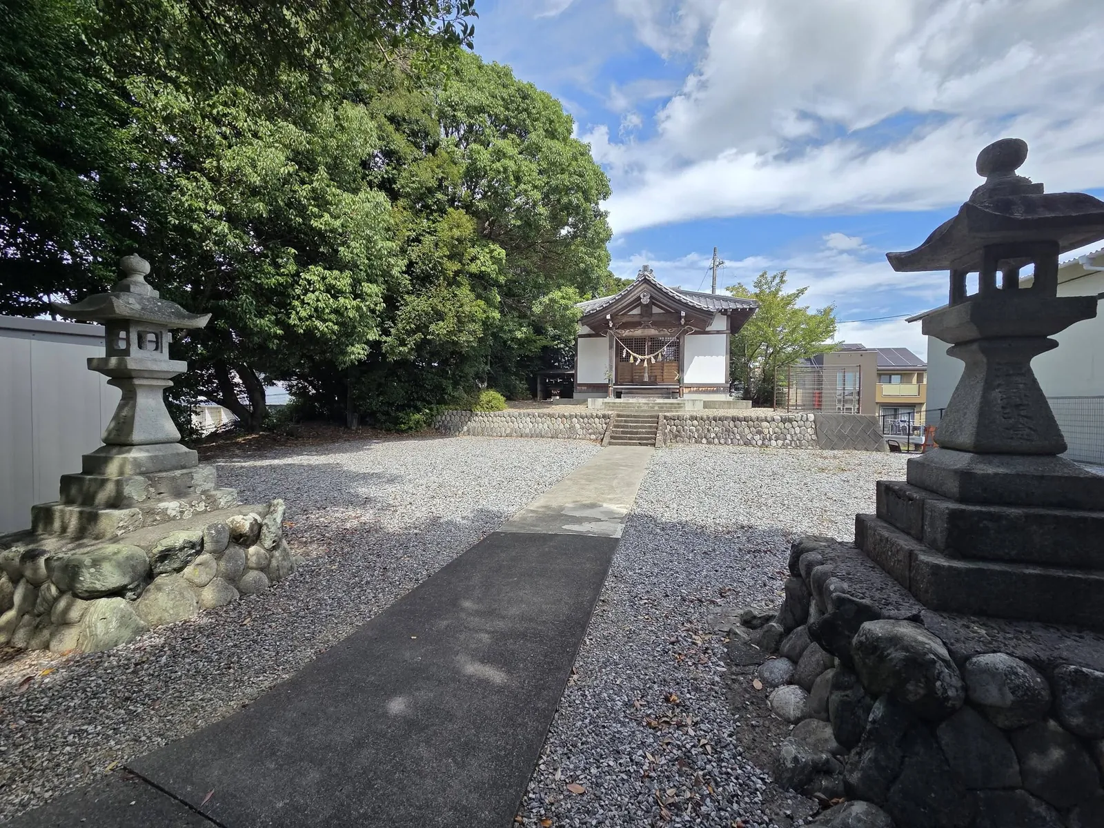 対の石灯籠の間から見た社殿。奥に隣接する住宅地が見える。