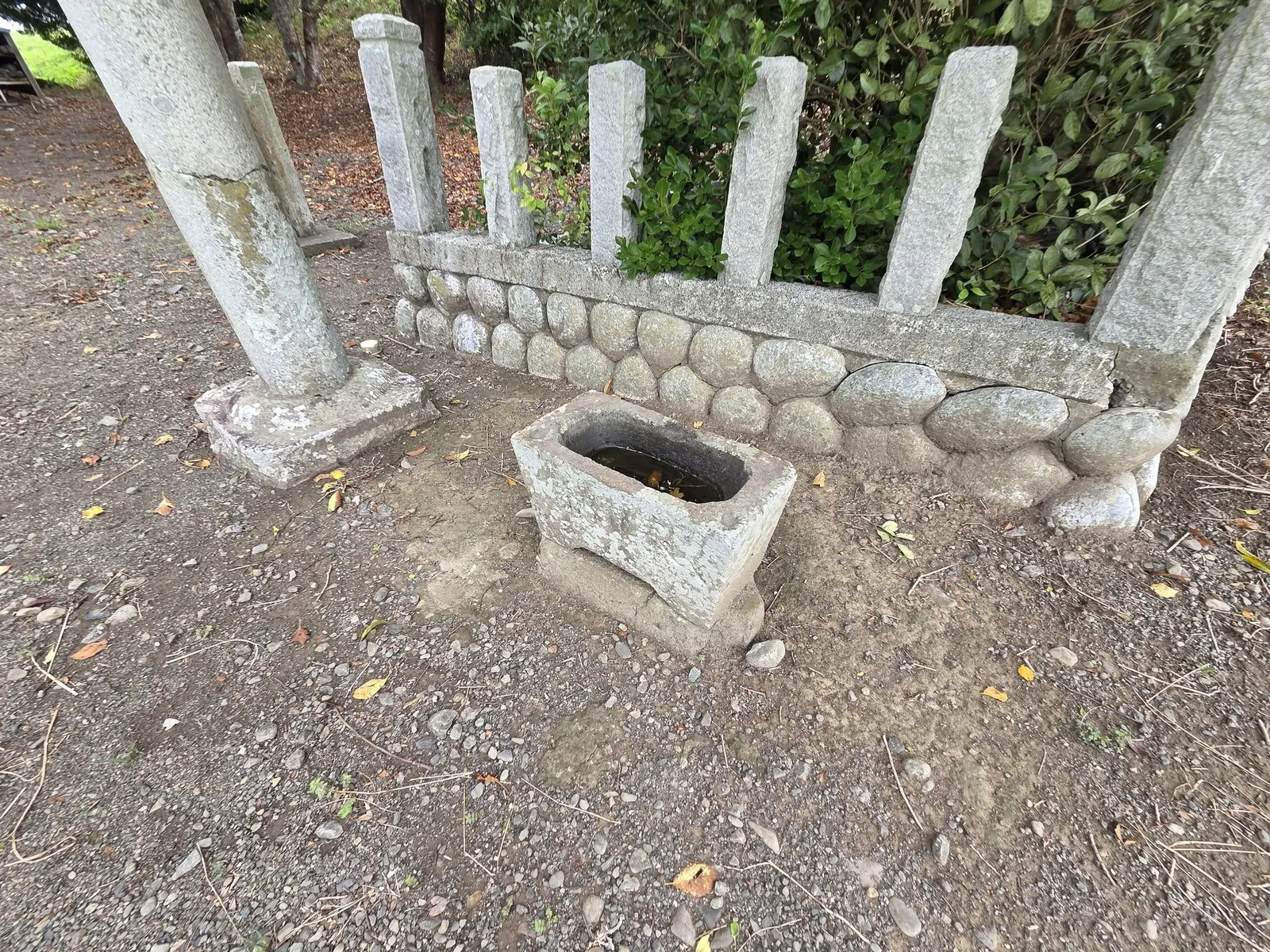 鳥居脇の石造手水鉢。背後の斜面には玉垣の石柱が並ぶ。