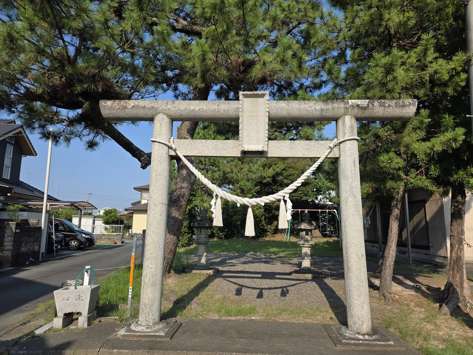 境内入口の石造鳥居。注連縄を張り、額束に石額を掲げる。左手前は手水鉢、参道の先に石灯籠が立つ。