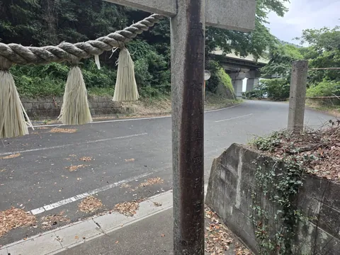 注連縄を掛けた石造鳥居と道路側の景観。
