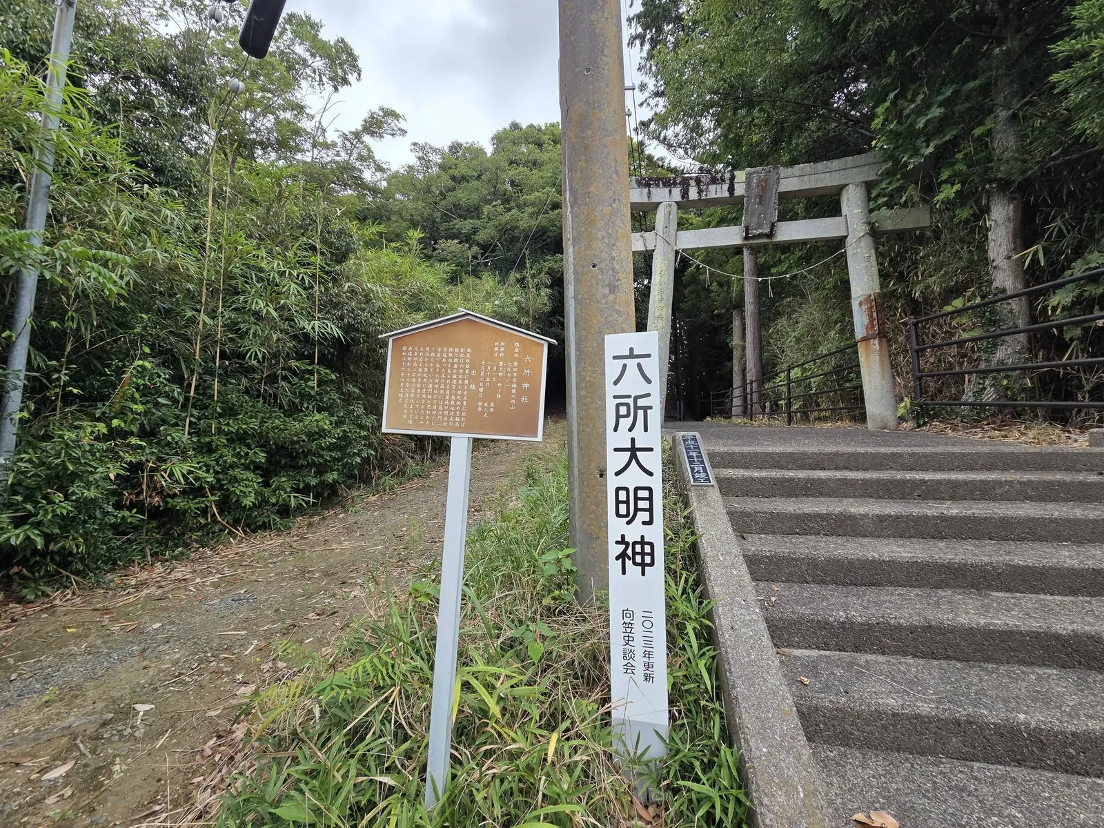 境内入口の石造鳥居と案内板。「六所大明神」の標柱が立つ。