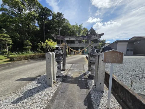 参道入口の石造鳥居。手前に灯籠と由緒板、奥に社叢が広がる。