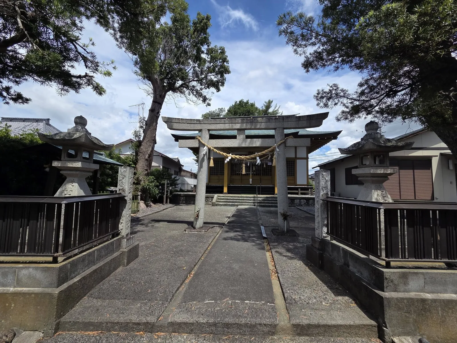 一対の石灯籠に挟まれた石造鳥居を参道正面から見る。注連縄の奥に社殿が見える。