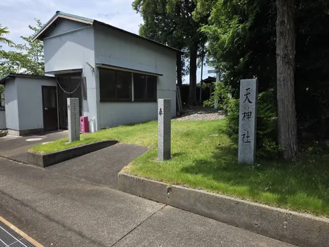 道路から見た境内入口。社号標「天神社」と社叢の大木が立つ。