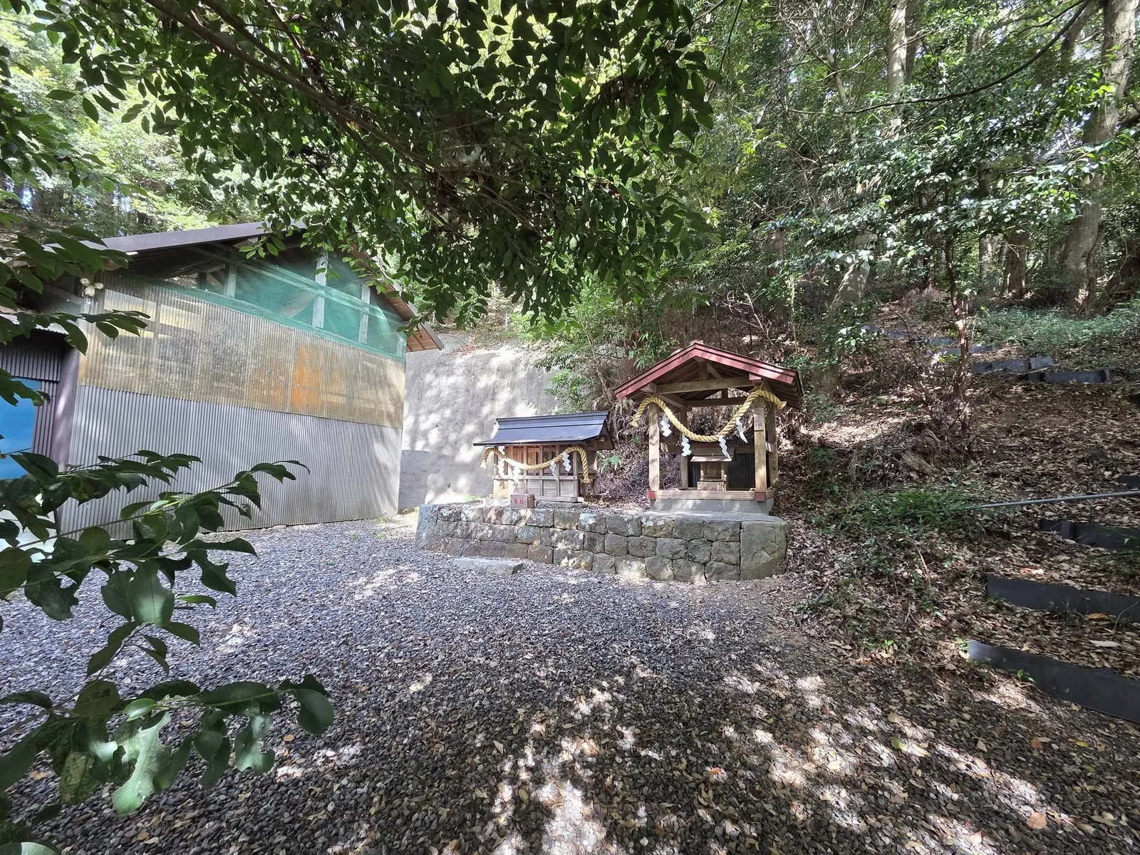 石垣の上に並ぶ二基の境内社。いずれも小さな覆屋に納められ、注連縄を掛ける。