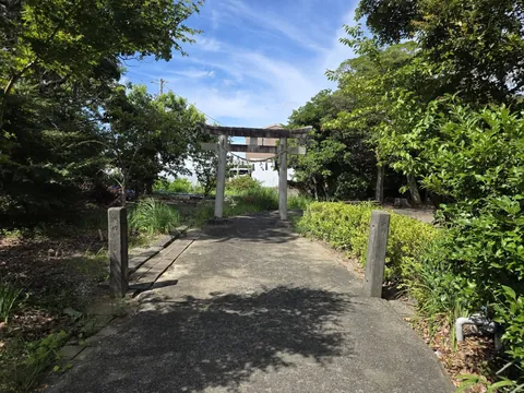 参道正面から見た石造の鳥居。注連縄と紙垂が下がり、奥に民家の屋根がのぞく。