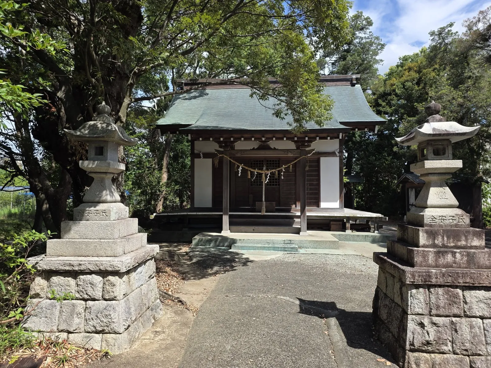 一対の石灯籠を前景にした社殿正面。緑青屋根と木立に囲まれた社殿全体を望む。